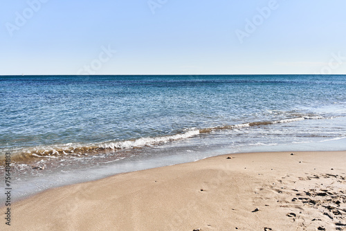 Tranquil beach scene with clear blue sky, golden sand, turquoise sea, and no people, depicting a serene holiday destination.