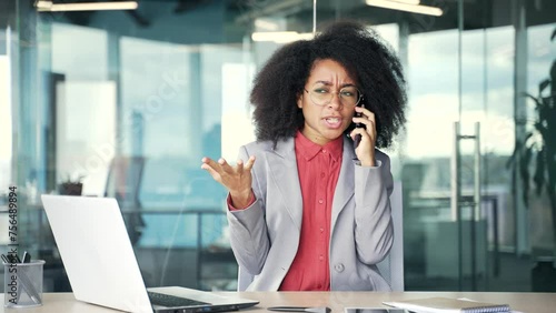Angry african american businesswoman arguing talking on mobile phone while sitting at workplace in business office. Frustrated black woman quarrels with subordinate describing problems on smartphone photo