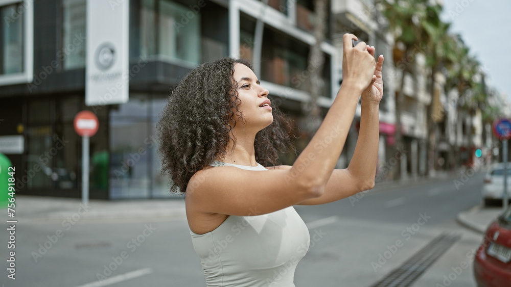 Young beautiful hispanic woman taking picture by the smartphone at street