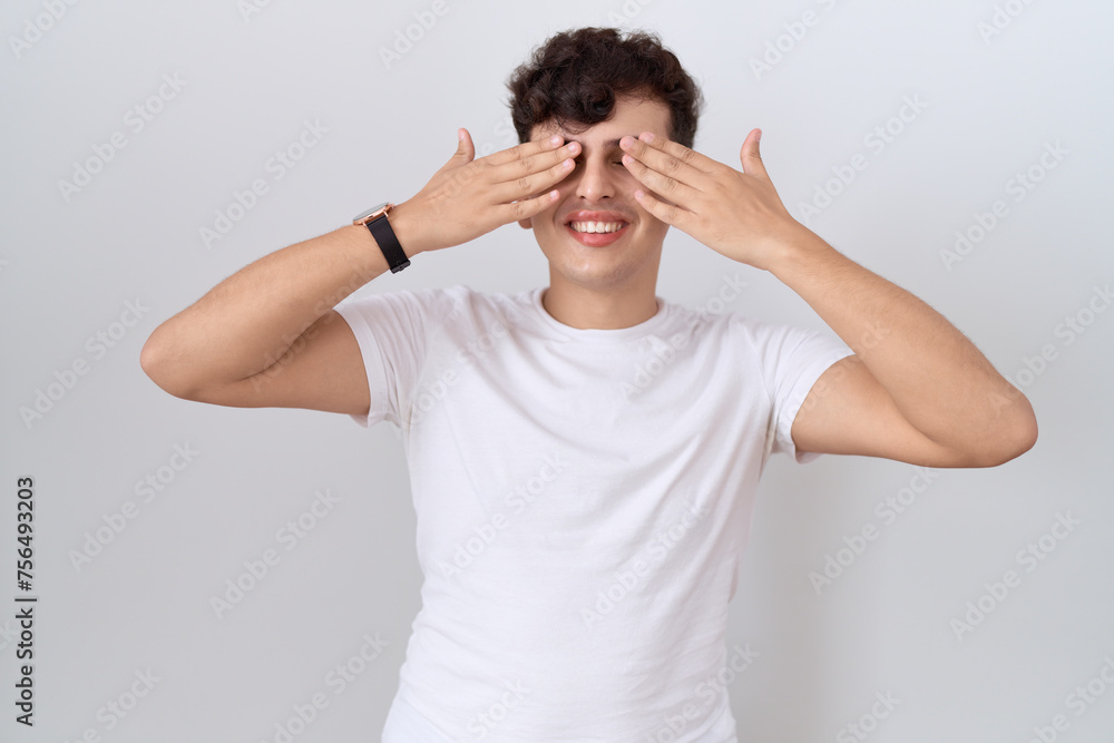 Young non binary man wearing casual white t shirt covering eyes with hands smiling cheerful and funny. blind concept. Young non binary man wearing casual white t shirt covering eyes with hands smiling cheerful and funny. blind concept.