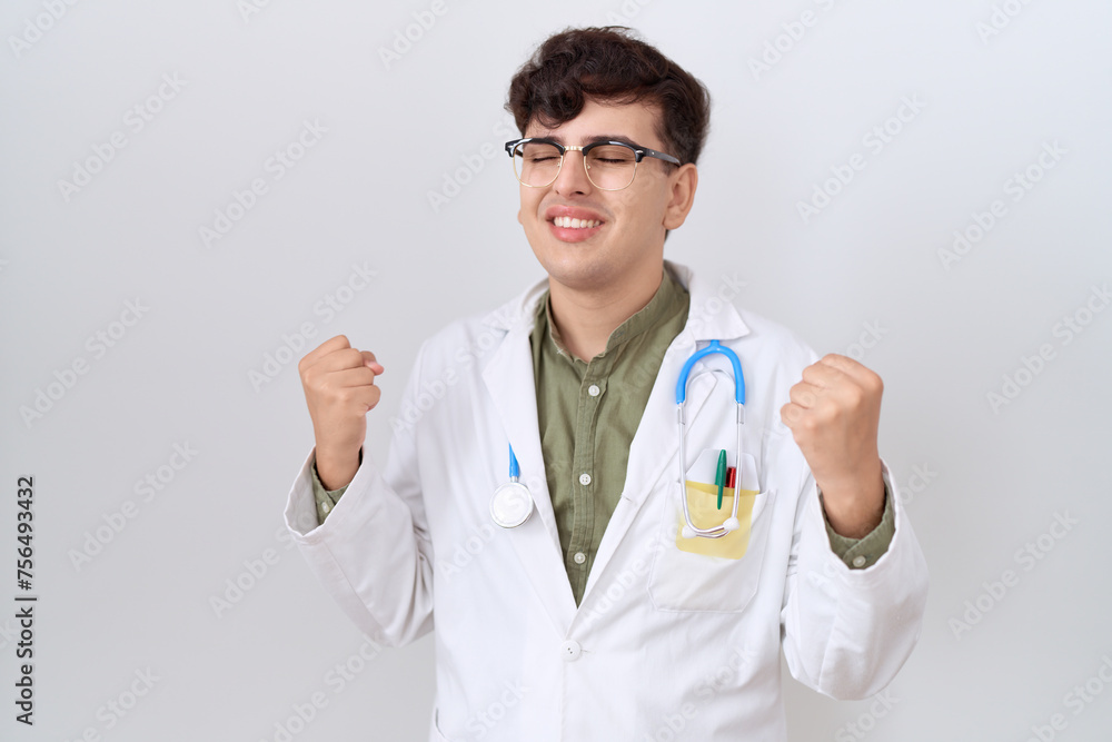 Young non binary man wearing doctor uniform and stethoscope very happy and excited doing winner gesture with arms raised, smiling and screaming for success. celebration concept. Young non binary man wearing doctor uniform and stethoscope very happy and excited doing winner gesture with arms raised, smiling and screaming for success. celebration concept.