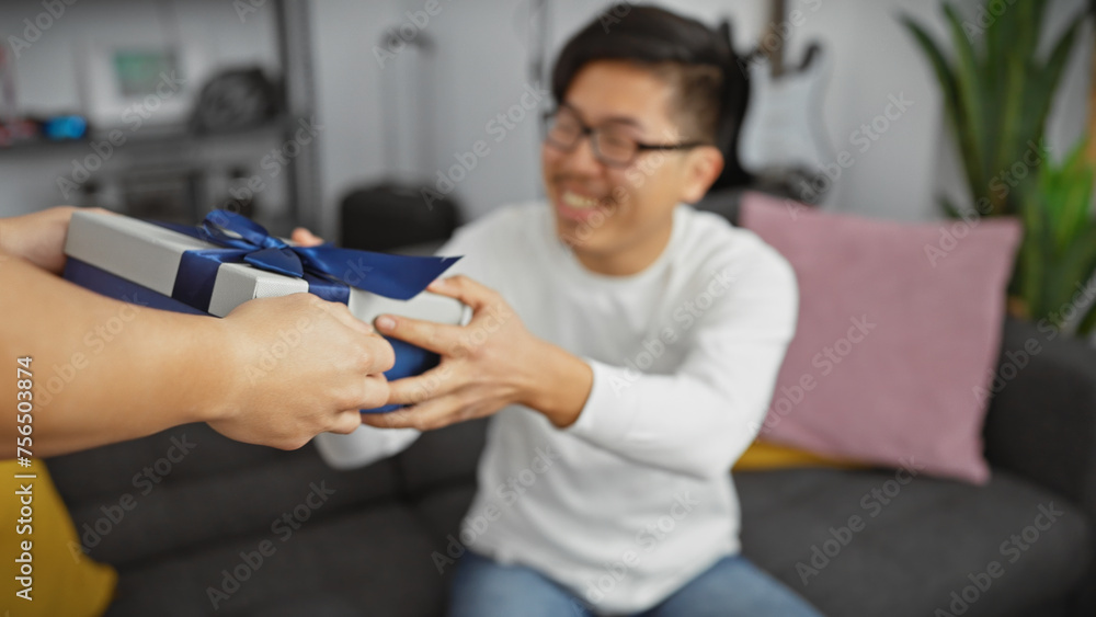 Fototapeta premium An asian man excitedly receiving a gift from another person in a cozy living room setting.