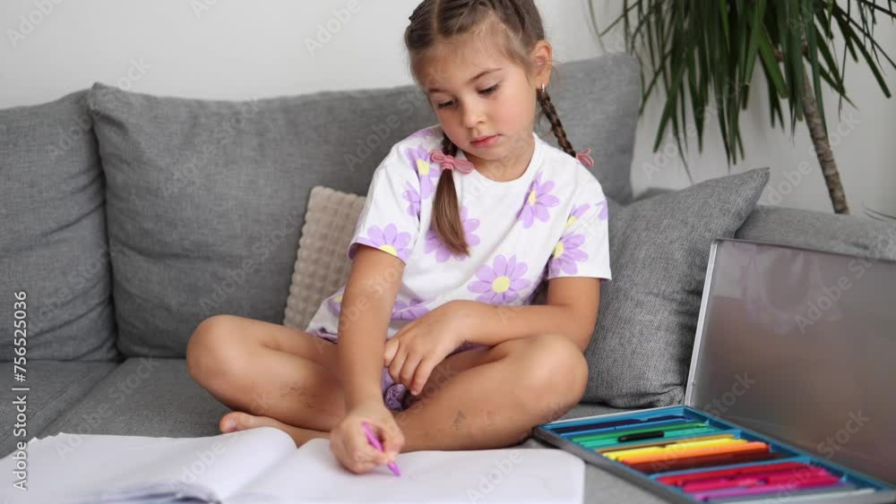 Cute little girl sitting on sofa in living room and draws by colored pencils. Home mood. Braid hairstyle Cute little girl sitting on sofa in living room and draws by colored pencils. Home mood. Braid hairstyle