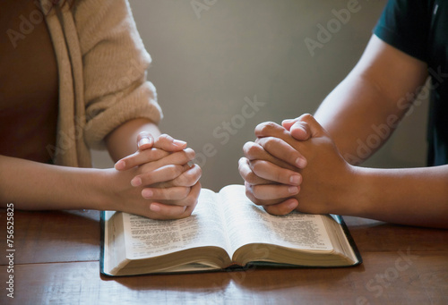 Woman and man praying and placing their hands on the bible bible.