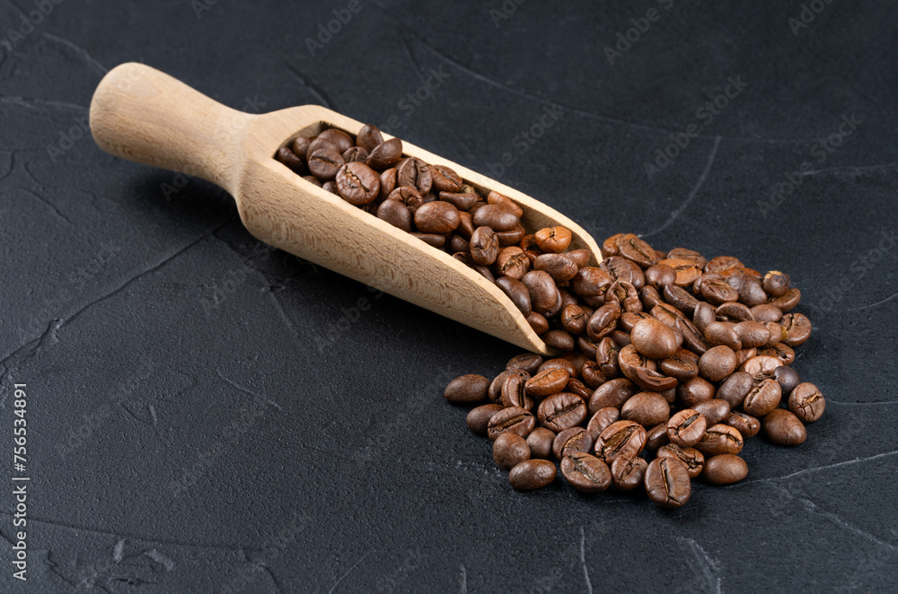 Obraz premium Loose roasted coffee beans from a wooden scoop on a dark background