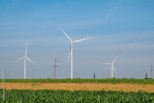 Windmills with rotating rotor blades on wheat field on sunny day. Countryside field with wind turbines producing alternative energy