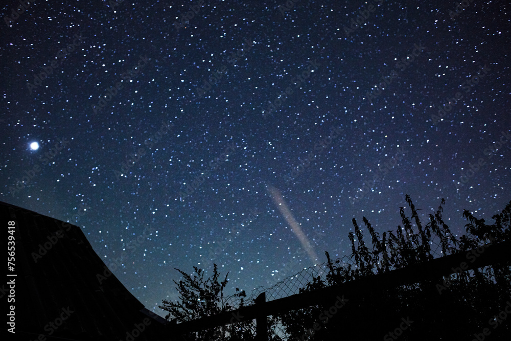 Starry sky with bright stars outside the city in the mountains, no one is there. Silhouettes of the roof and fence.