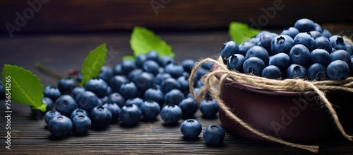 A bowl of electric blueberries with leaves on a wooden table, showcasing the beauty of natural foods and superfoods in still life photography