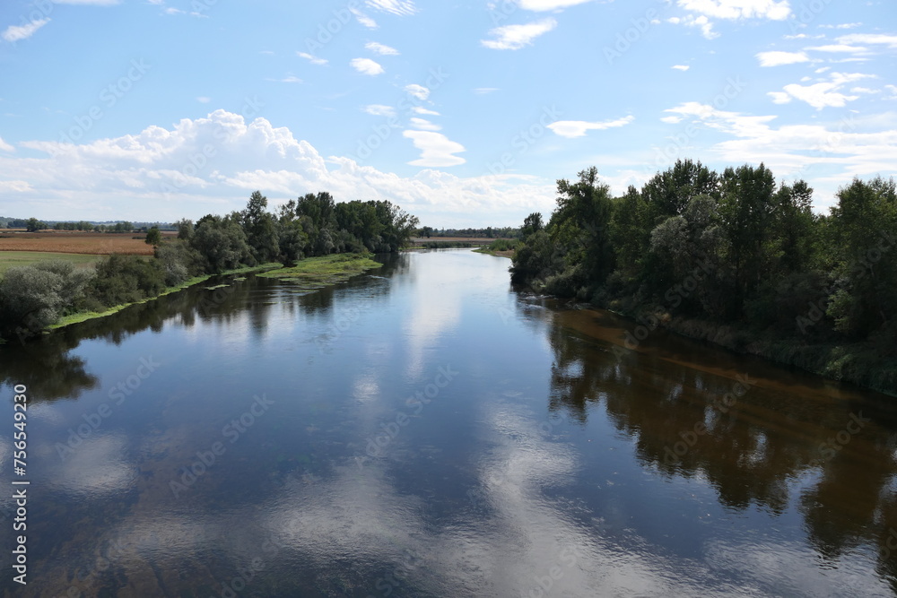 A horizontal view of a serene river in France during the summer. The water is low, and trees line the riverbanks, their vibrant green foliage reflected in the calm waters. A horizontal view of a serene river in France during the summer. The water is low, and trees line the riverbanks, their vibrant green foliage reflected in the calm waters.
