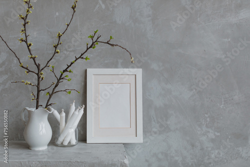 Blank picture frame next to cherry plum branches in a jug and candles on a mantelpiece photo
