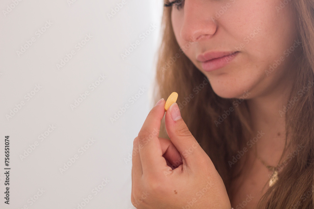 Concept of suffering from terrible pain. Beautiful, sad, upset, unhappy, troubled, weak woman with blonde hair, wearing casual clothes is sitting on a sofa and taking a pill