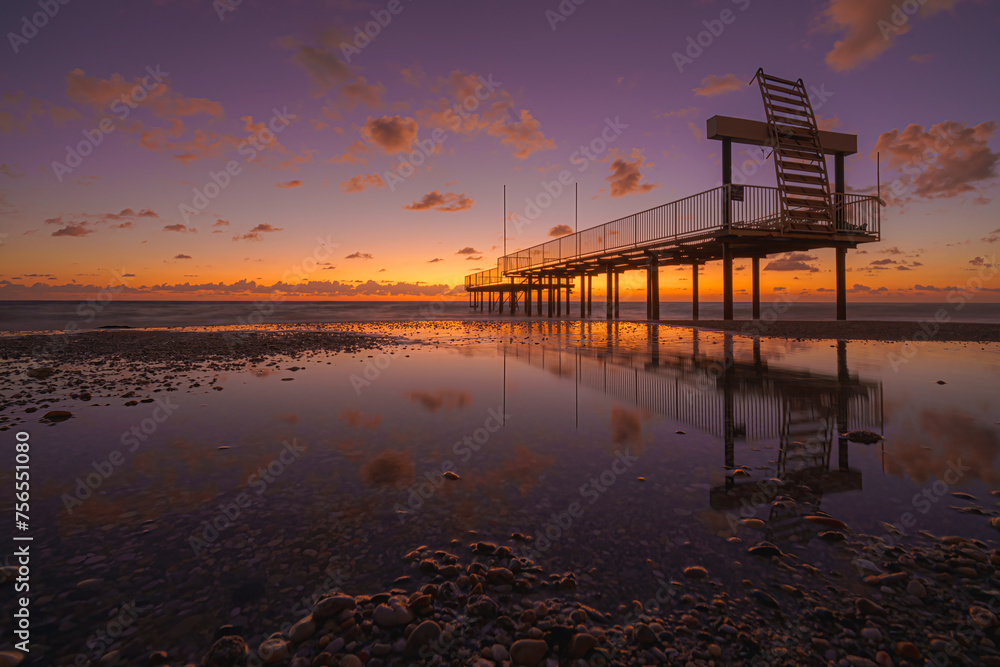 Alanya, Antalya, Türkiye, Turkey, Panoramic view of the Mediterranean Sea, low tide, wooden pier reflected in the water, at sunset with a blue and orange sky and clouds, at evening 