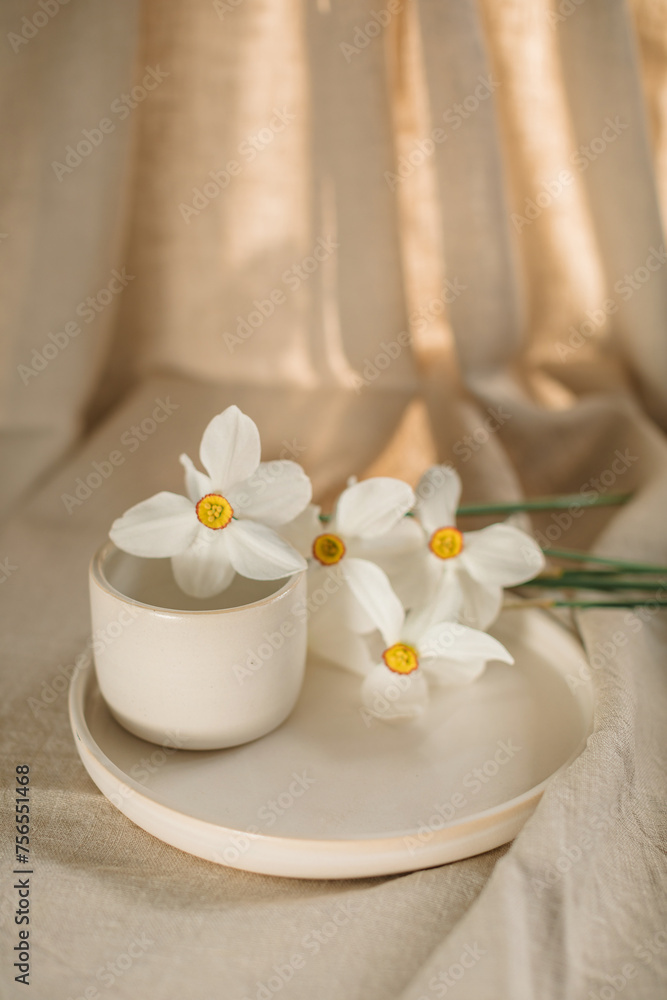 White narcissus flowers with a ceramic plate and cup on a table White narcissus flowers with a ceramic plate and cup on a table