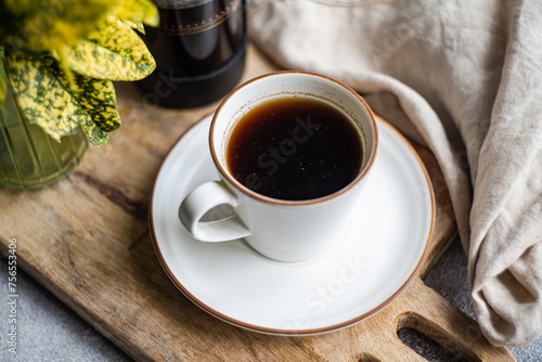 Close-up of a cup of black coffee on a chopping board with a cafetiere, napkin and foliage