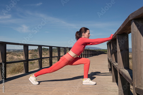 Sporty woman doing a leg stretch warm up exercise outside on a boardwalk