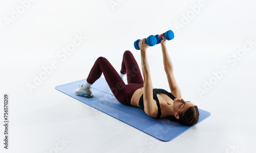 Young woman with slim, fit body in sportswear training on fitness mat, lifting dumbbells, isolated on white studio background. Concept of sport, health and body care, fitness app, exercises templates