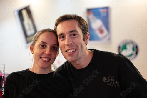 Portrait of a smiling and happy wedding couple in a cocktail bar. They are both smiling, they are dressed in black. There is bokeh in the background