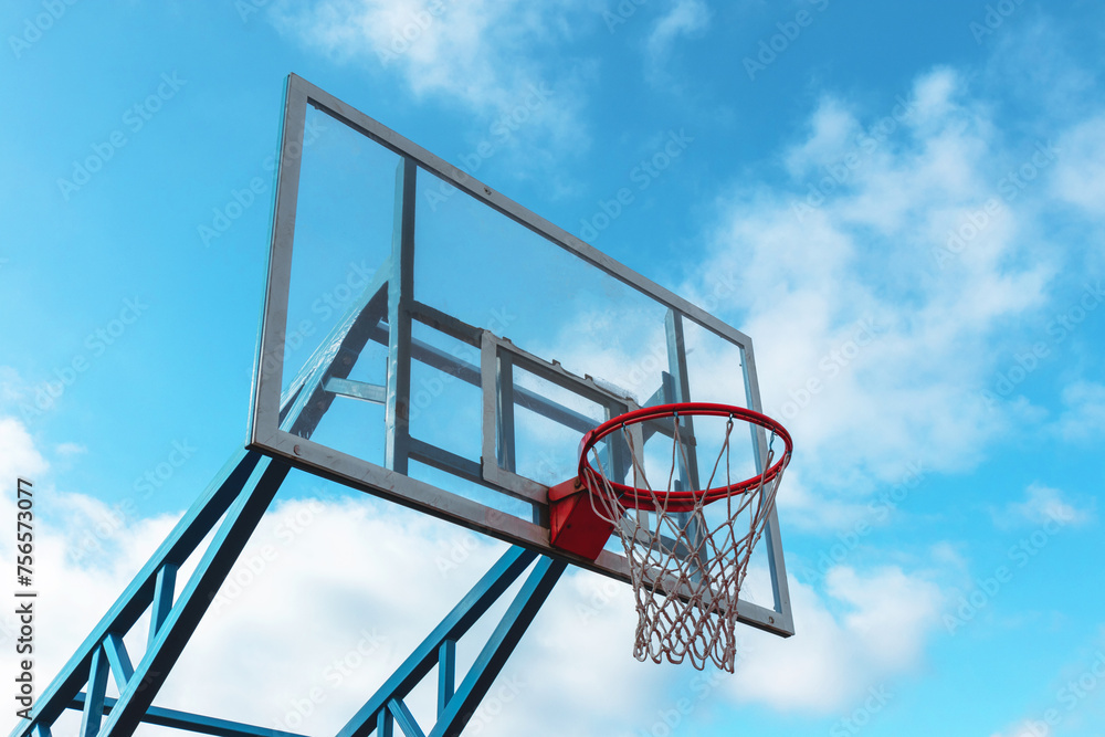Red basketball hoop with a glass backboard against a blue sky