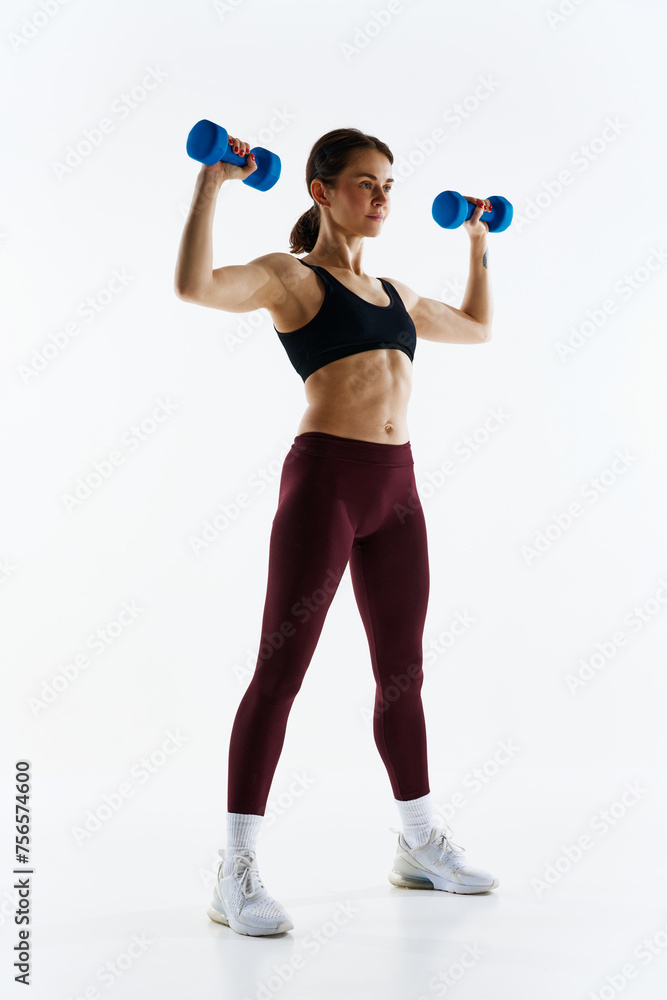 Young woman with sportive, muscular fit body in leggings and top training with dumbbells isolated over white studio background. Concept of sport, health and body care, fitness app, exercises templates Young woman with sportive, muscular fit body in leggings and top training with dumbbells isolated over white studio background. Concept of sport, health and body care, fitness app, exercises templates