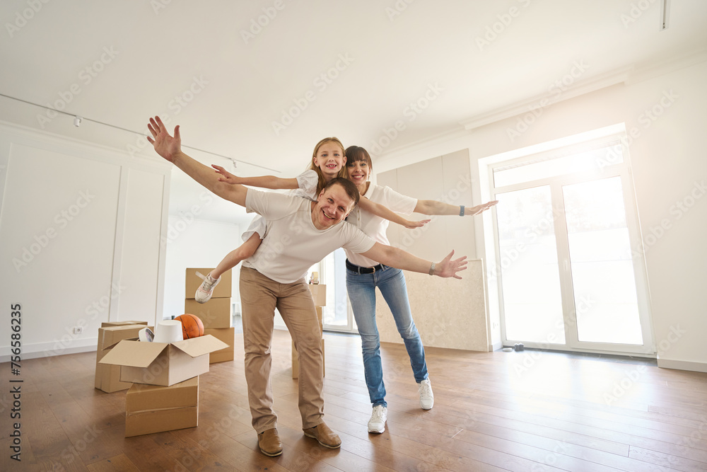 Happy family posing like flying birds and looking at camera in new townhouse Happy family posing like flying birds and looking at camera in new townhouse