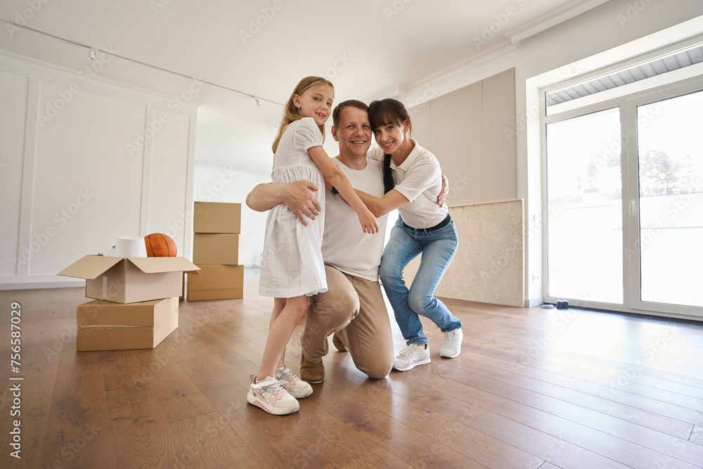 Joyful family embracing and looking at camera in new sunny modern townhouse Joyful family embracing and looking at camera in new sunny modern townhouse