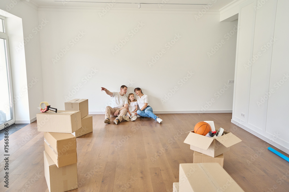 Man showing something to wife and daughter on floor in townhouse during moving Man showing something to wife and daughter on floor in townhouse during moving