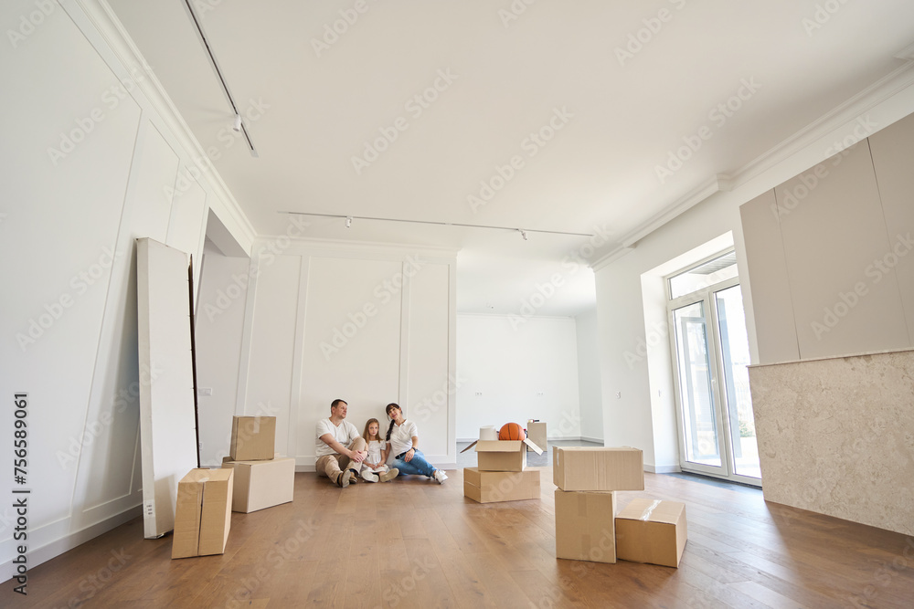 Fototapeta premium Serious caucasian family on floor looking at new modern townhouse during moving