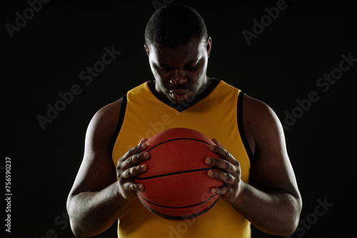 Dramatic waist up portrait of muscular basketball player holding ball to chest with backlight outline copy space