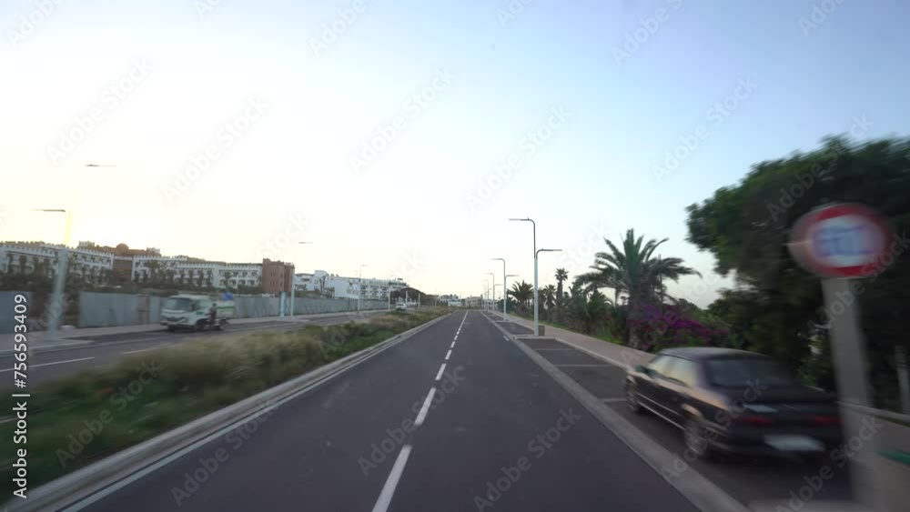 Agadir, Morocco - February 25, 2024 - Roadway view from a bus, showing an empty street flanked by buildings and palm trees under a clear sky at dusk or dawn Agadir, Morocco - February 25, 2024 - Roadway view from a bus, showing an empty street flanked by buildings and palm trees under a clear sky at dusk or dawn