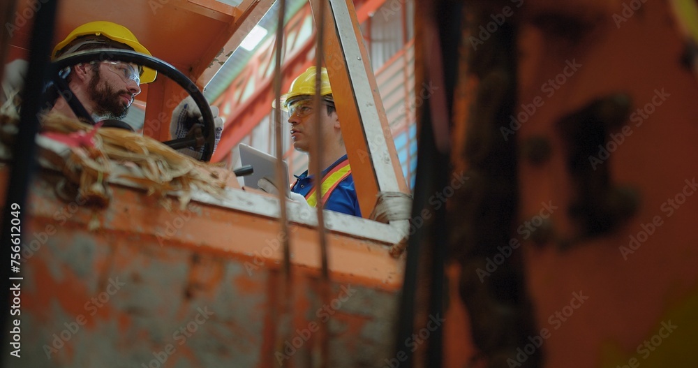 Construction workers in yellow hard hats and safety vests operate a construction lift machinery within an industrial environment, focus on occupational safety and teamwork