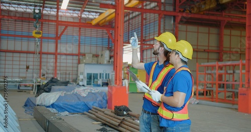 Two construction workers in reflective vests and hard hats consulting over a clipboard in an industrial warehouse, symbolizing teamwork and project planning