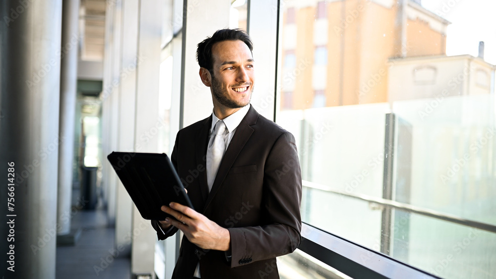 Fototapeta premium Smiling businessman with tablet at modern office corridor