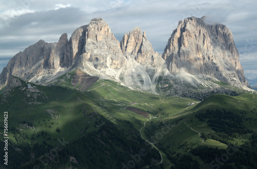 Landscape photo with a view of the Sassolungo mountain massif partially covered by clouds and illuminated by the morning sun in the Dolomites, South Tyrol region, Italy