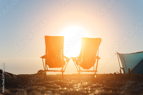 Two folding camping chairs against the backdrop of the setting sun. Camping tourism. Nobody