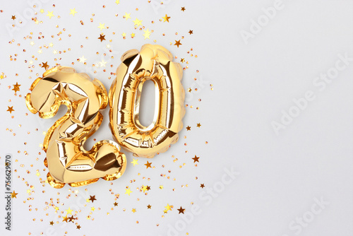 Number twenty golden foil balloons with stars confetti on a blue background.