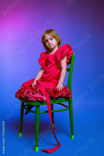 little girl sitting on a chair in a pink suit on a blue background © TanyaMedvedeva