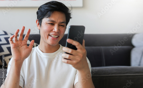close up young asian man using video call form smartphone to talking with friends and family at living room in home for modern lifestyle concept