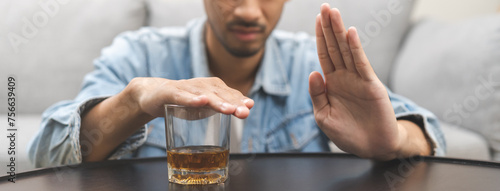 Alcoholism, depressed asian young man refuse, push out alcoholic beverage glass, drink whiskey, sitting alone at night. Treatment of alcohol addiction, having suffer abuse problem alcoholism concept. photo