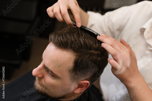 Haircut of a visitor in a barbershop. Hair styling with a comb, combing the client's hair by a stylist.