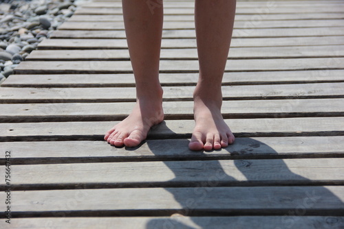 Bare feet of a child close-up on a wooden board on the beach © Екатерина Шведова