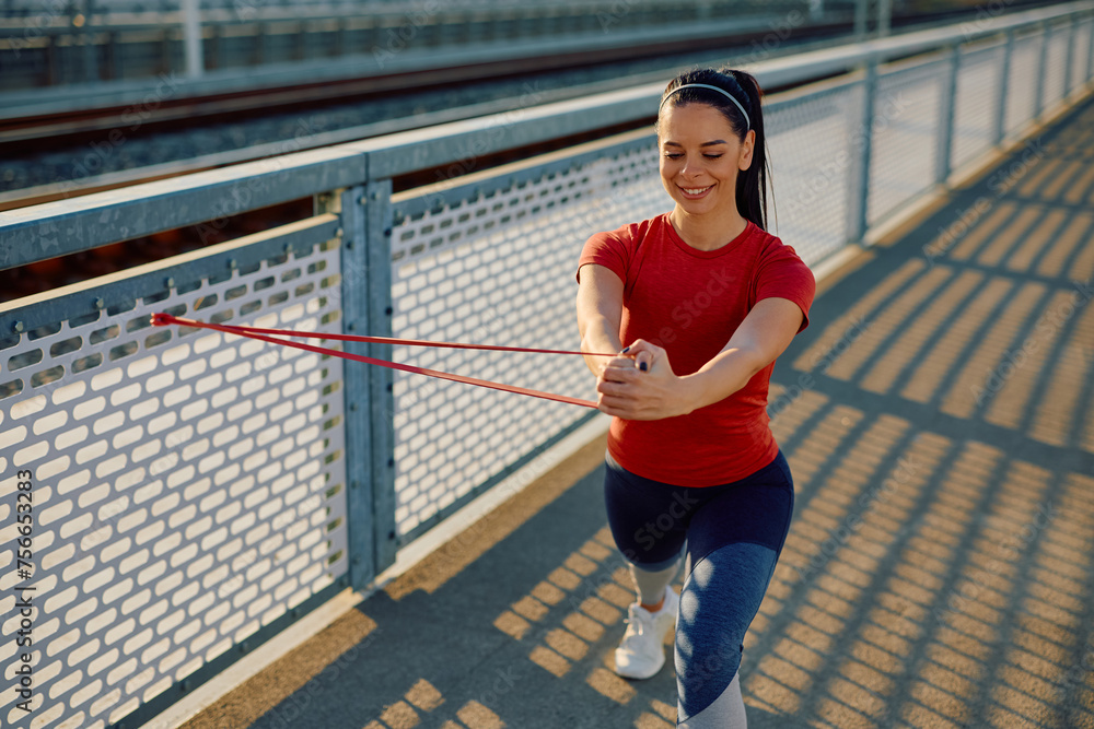 Young happy sportswoman using power band while exercising outdoors