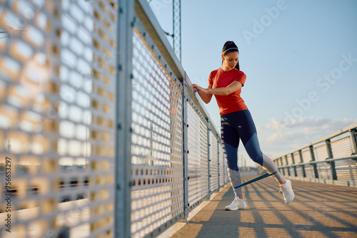 Athletic woman doing leg exercises with resistance band outdoors.