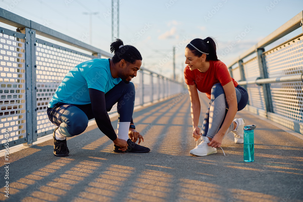 Happy athletes tying shoelaces on sneakers while working out outdoors.
