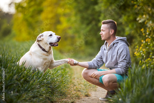 Happy man with dog in nature on sunny summer day. Cute yellow labrador retriever giving paw to his pet owner..