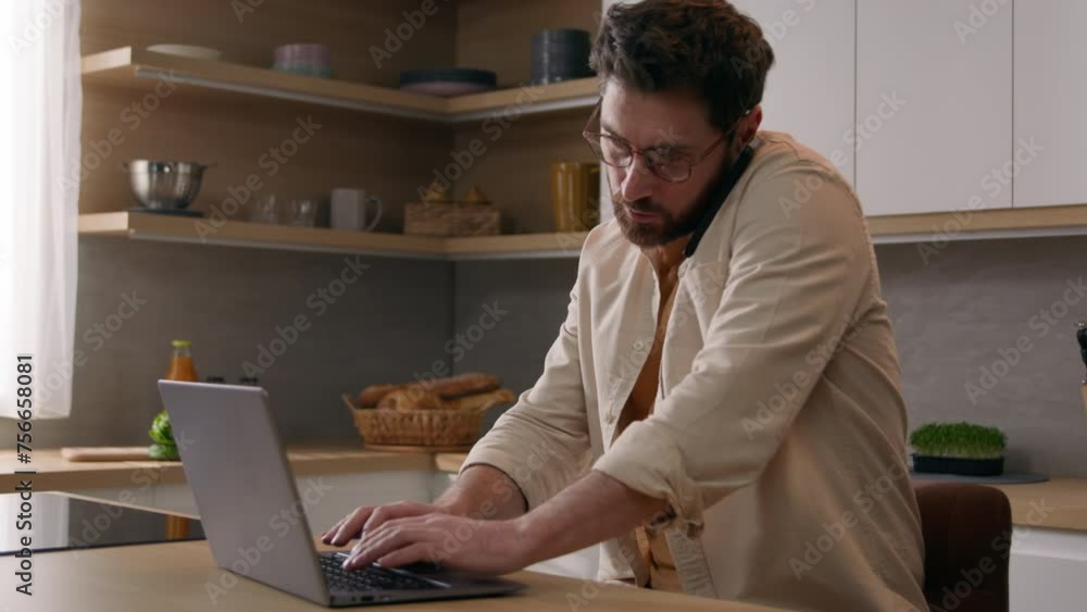 Male freelancer businessman at table with laptop in modern kitchen discussing project with mobile phone call distant work from home. 40s man homeowner talking smartphone browsing computer multitasking Male freelancer businessman at table with laptop in modern kitchen discussing project with mobile phone call distant work from home. 40s man homeowner talking smartphone browsing computer multitasking