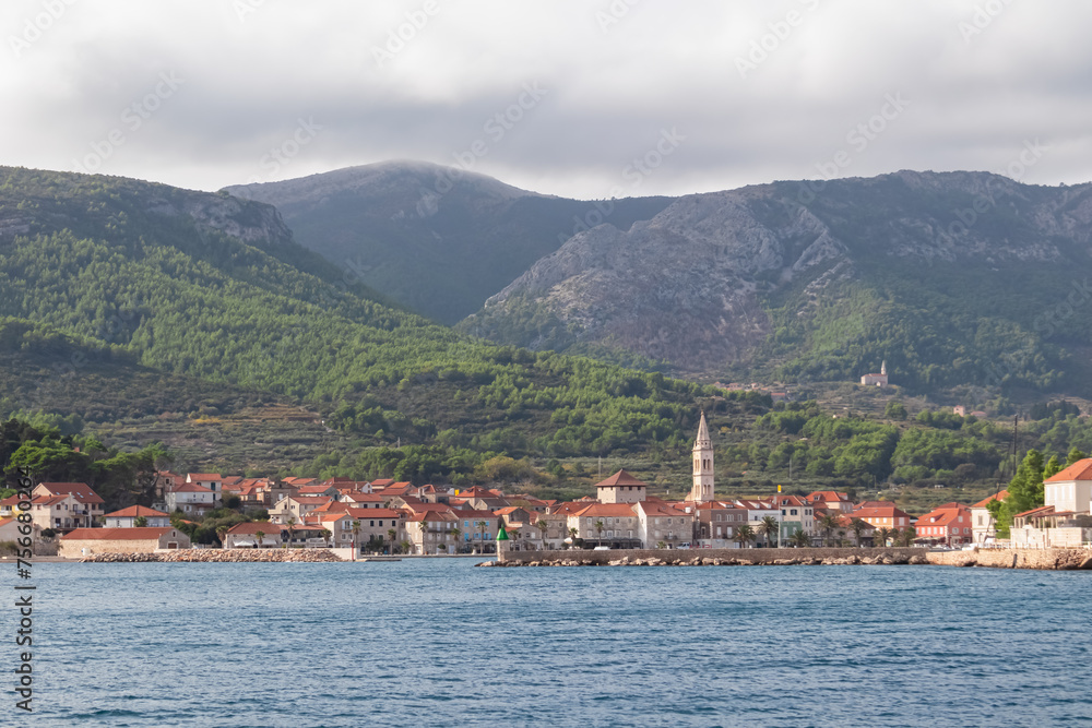 Scenic view of coastal town Jelsa on Hvar island in Dalmatia, South Croatia, Europe. Coastline of Adriatic Sea seen from boat tour in Balkans. Arriving in idyllic port in Mediterranean architecture