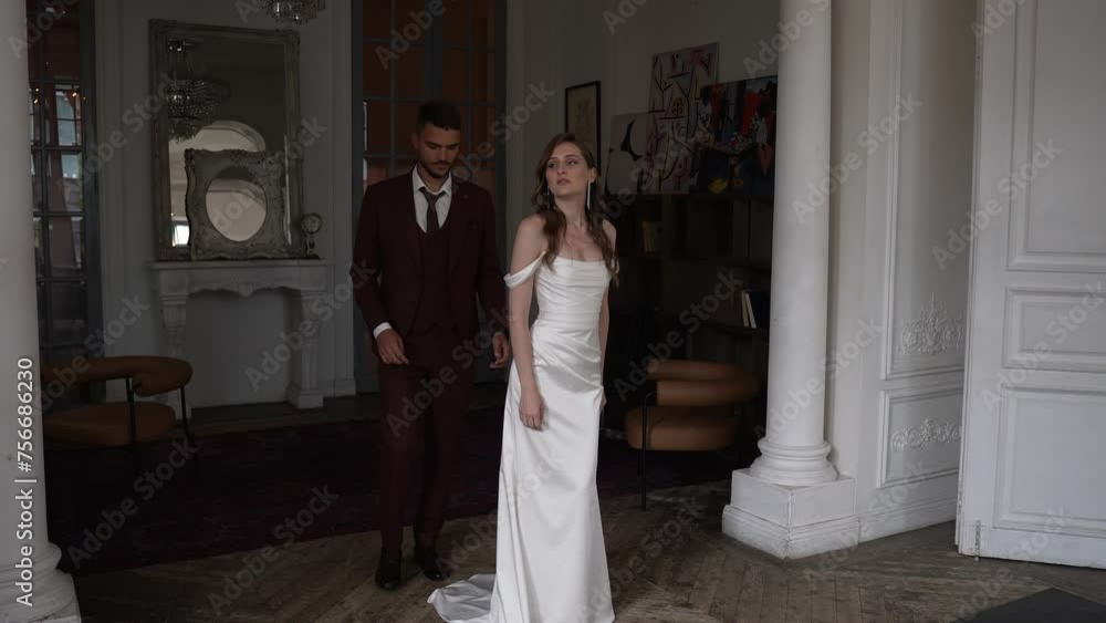 Bride and groom in bridal clothing stand beside each other in a room Bride and groom in bridal clothing stand beside each other in a room