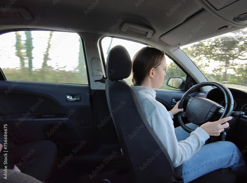 Young traveler girl driving her grand tourer car on the roads. She is driving attentively with her hands on the wheel, it is daytime and she is driving a very large car. Interior view Young traveler girl driving her grand tourer car on the roads. She is driving attentively with her hands on the wheel, it is daytime and she is driving a very large car. Interior view