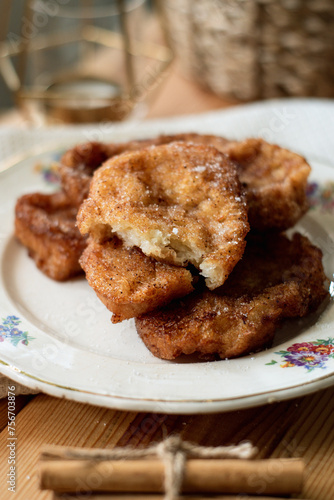 White plate with a torrija, typical dessert of the spanish holy week, it is fried bread with sugar. With some branches of cinnamon on a wood.