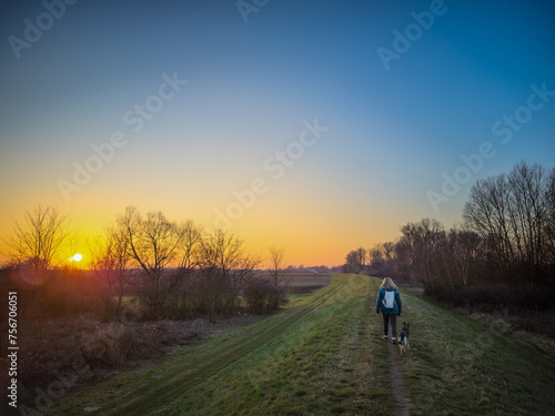Adult woman walking her dog on the embankment at sunset.  © PatPat